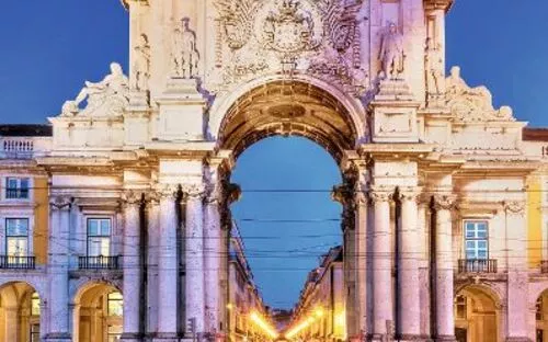 Historischer Triumphbogen bei Dämmerung mit beleuchteter Straße im Hintergrund.