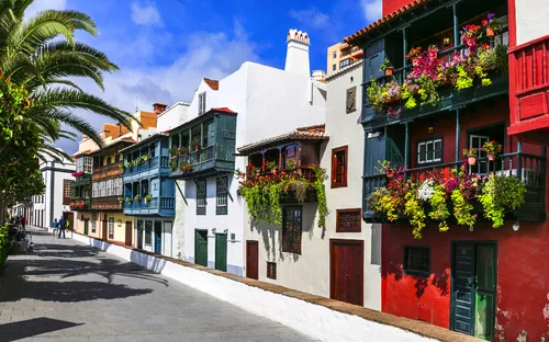 Bunte Häuserfassaden mit Blumenbalkonen in einer Straße bei Sonnenschein.