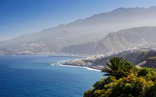 Küstenlandschaft mit Bergen, Meer und einem kleinen Ort im Vordergrund.