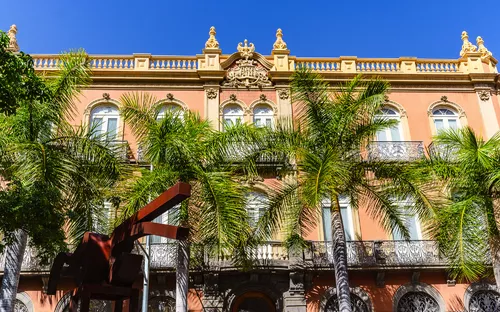 Historisches Gebäude mit Palmen im Vordergrund bei klarem Himmel.