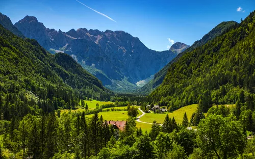 Blick auf ein grünes Tal mit Bergen im Hintergrund bei klarem Himmel.