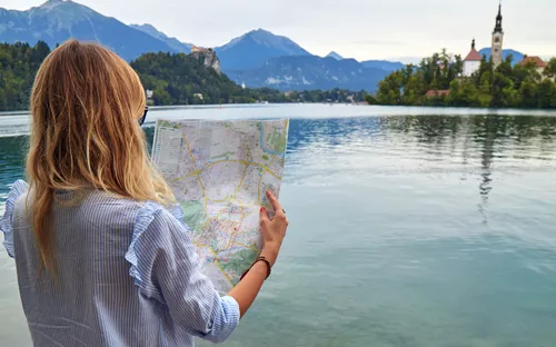 Frau betrachtet Karte am Seeufer mit Schloss und Kirche im Hintergrund.