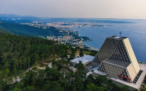 Luftaufnahme einer modernen Kirche mit Blick auf eine Küstenstadt und das Meer im Hintergrund.