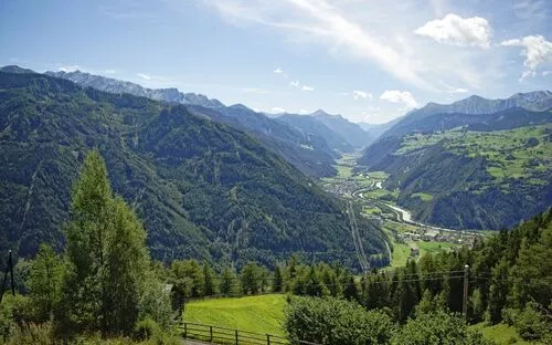 Blick auf ein alpines Tal mit grünen Hängen und klarem Himmel.