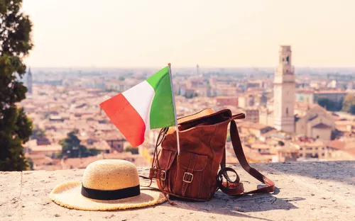 Hut, Rucksack und italienische Flagge vor Stadtpanorama.
