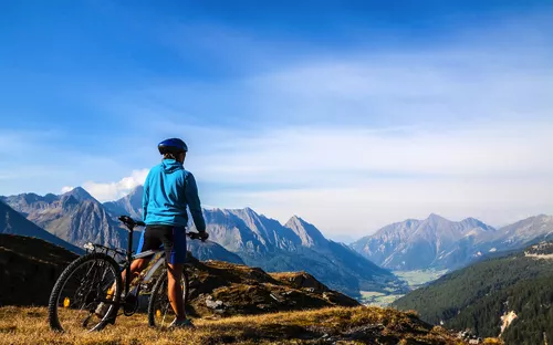 Person mit Fahrrad schaut auf Berglandschaft.