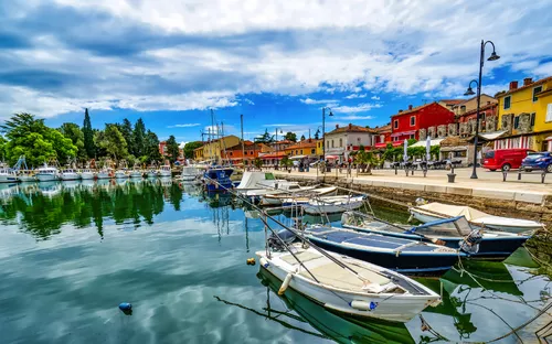 Boote an einem ruhigen Hafen mit bunten Gebäuden und Wolken am Himmel.