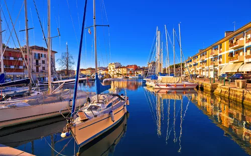 Segelboote im Hafen, sonniger Tag, ruhiges Wasser, Gebäude im Hintergrund entlang des Kais.