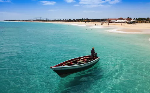 Boot auf türkisfarbenem Meer, Sandstrand im Hintergrund, klarer blauer Himmel.