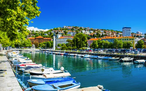 Uferpromenade mit Booten, blauen Himmel, und Stadt im Hintergrund.