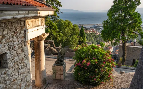 Steinbalkon mit Blick auf das Meer, umgeben von Bäumen und historischen Gebäuden.