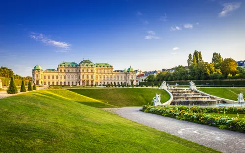 Barockes Schloss mit Gartenanlage und Springbrunnen bei Sonnenuntergang.