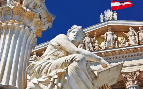Statue vor einem klassizistischen Gebäude mit Säulen, im Hintergrund eine österreichische Flagge.