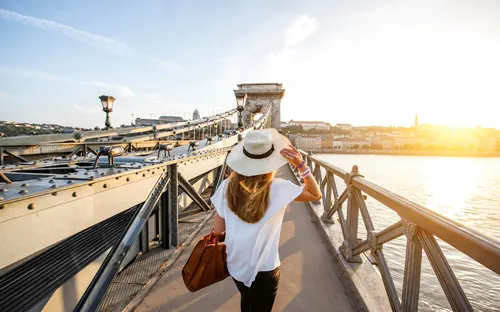 Frau mit Hut geht über eine Brücke bei Sonnenuntergang.