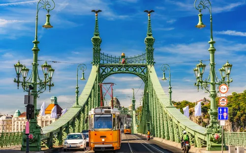 Grüne Brücke mit gelber Straßenbahn und Fußgängern am Tag.
