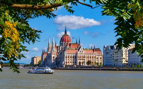Parlamentsgebäude von Budapest, Ungarn, am Ufer der Donau, umrahmt von Bäumen im Vordergrund.