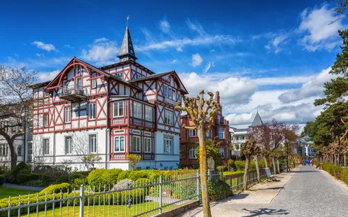 Fachwerkhaus an einer Allee mit blauen Himmel im Hintergrund.