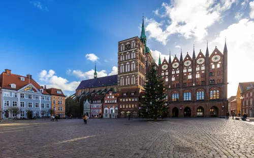 Marktplatz mit historischem Gebäude und Weihnachtsbaum bei klarem Himmel.