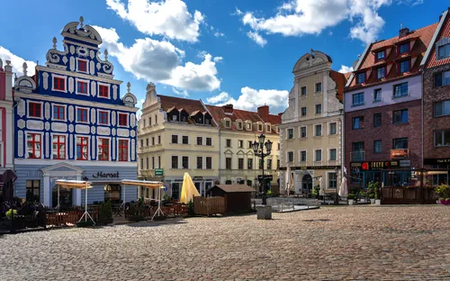 Historischer Marktplatz mit bunten Gebäuden und wolkigem Himmel.