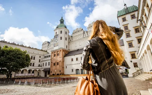 Frau betrachtet ein historisches Schloss auf einem sonnigen Platz.