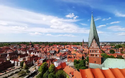 Stadtpanorama mit Kirchtürmen und roten Ziegeldächern unter blauem Himmel.