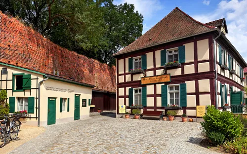 Fachwerkhaus mit grünen Fensterläden und Kopfsteinpflasterstraße bei sonnigem Wetter.
