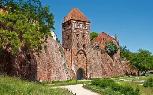 Historische Backsteinburg mit Rundturm und grünem Park im Vordergrund.