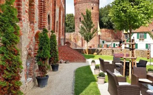 Backsteinbau mit Turm, Sitzbereich im Freien, sonnig, Baum und Topfpflanzen.