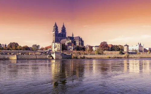 Fluss mit historischer Kathedrale und Stadtmauer bei Sonnenuntergang.