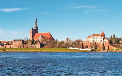Stadtansicht mit Kirche und historischen Gebäuden am Flussufer bei klarem Himmel.