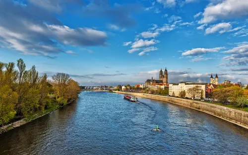 Fluss mit Boot, umgeben von Stadtlandschaft und bewölktem Himmel.