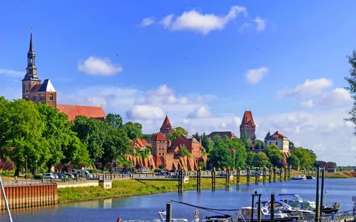 Stadtsilhouette mit Fluss, Booten und Kirche im Hintergrund unter blauem Himmel.
