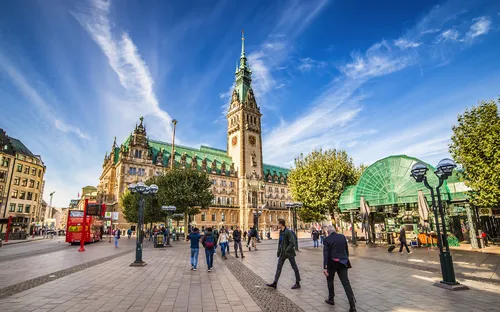 Menschen vor dem Rathaus in Hamburg bei sonnigem Wetter.