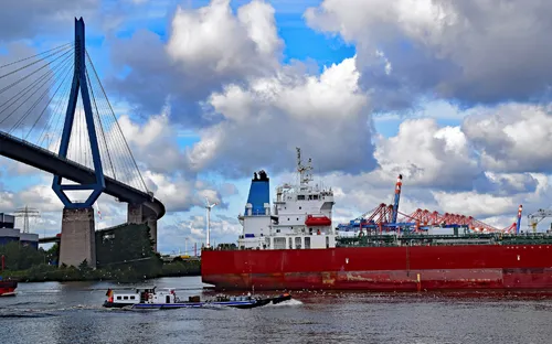 Großes Schiff auf einem Fluss nahe einer Brücke und einem Hafen.