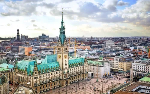 Blick auf das Hamburger Rathaus und den umliegenden Platz bei bewölktem Himmel.