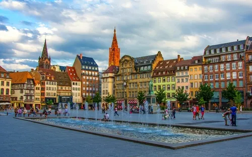 Historischer Platz mit Brunnen und Fachwerkhäusern bei bewölktem Himmel.