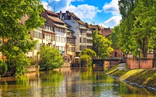 Häuserreihe am Flussufer mit Brücke und Bäumen bei sonnigem Wetter