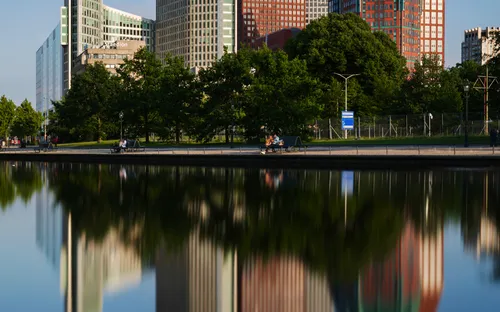 Moderne Gebäude mit Bäumen davor spiegeln sich im Wasser.