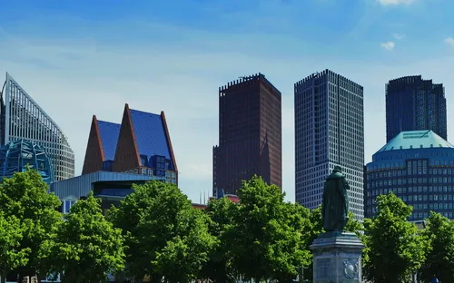 Moderne Skyline mit Bäumen und Statue im Vordergrund.