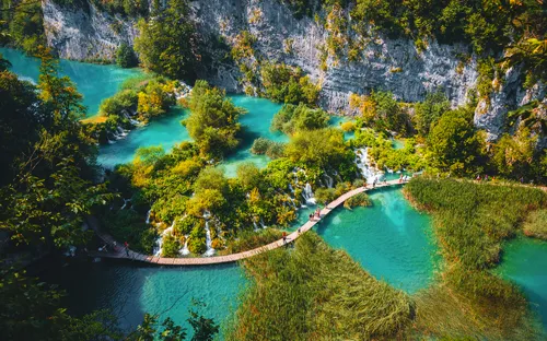 Holzsteg über türkisfarbenem See in bewaldeter Schlucht.