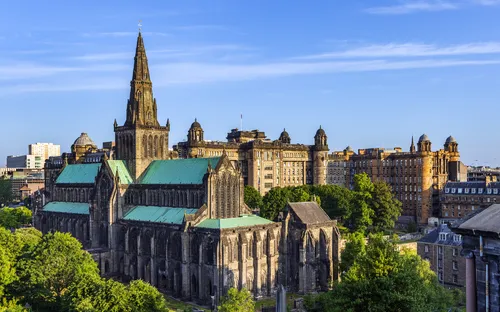 Glasgow Kathedrale in Schottland, umgeben von Stadtgebäuden und grünen Bäumen, bei klarem Himmel.
