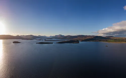 Panorama eines Sees mit Inseln und tiefstehender Sonne am Horizont.