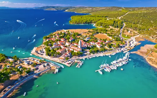 Luftaufnahme einer Küstenstadt mit Hafen und Booten im klaren, türkisfarbenen Wasser.