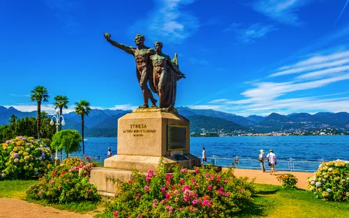 Statue vor einem See mit Bergen im Hintergrund bei klarem Himmel.