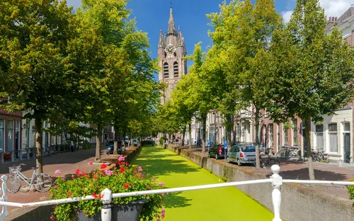 Kanal in Delft mit Bäumen und Kirche im Hintergrund bei sonnigem Wetter.