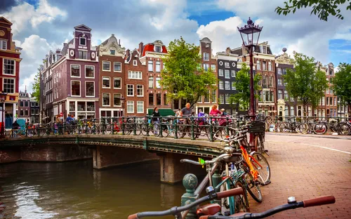 Kanal in Amsterdam mit Fahrrädern auf einer Brücke und typischen Giebelfassaden im Hintergrund.