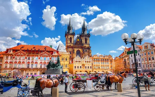 Historischer Platz mit Pferdekutschen und gotischer Kirche.