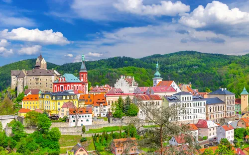 Panorama einer bunten, historischen Stadt vor bewaldeten Hügeln und blauem Himmel.