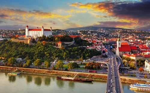 Stadtansicht von Bratislava mit Burg und Fluss bei Sonnenuntergang.