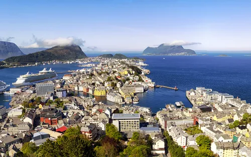Panorama einer Küstenstadt mit Kreuzfahrtschiffen und Bergen im Hintergrund.